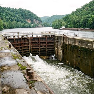 Concrete lock chamber and dam gates on a wide green river seen from a raised platform on a humid May morning