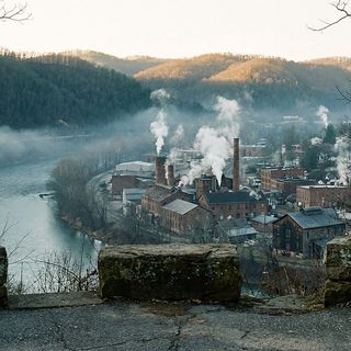 A wooded ridge overlook at dawn above a river valley with a city in shadow and bare winter hills beyond
